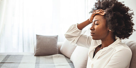 A woman sits with her eyes closed and her hand on her forehead.